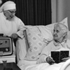 Thumbnail and detail of bedroom in a nursing home, in black and white. An elderly woman in the bed, with a book, smiling. There's a nun in habit at bedside, also smiling, with a radio in front of her.