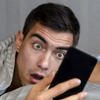 Young adult man looking at his smart phone with a shocked, surprised but slightly comical expression.