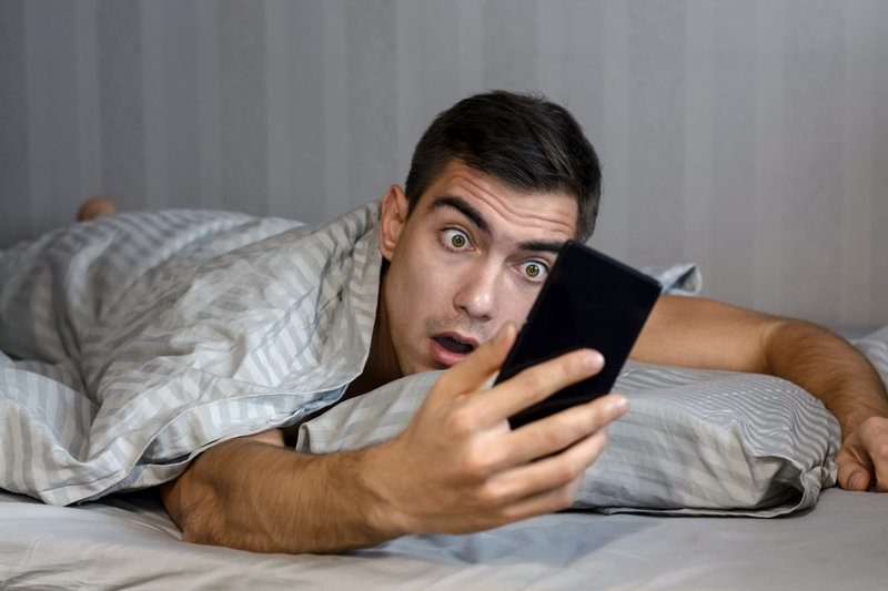 Young adult man looking at his smart phone with a shocked, surprised but slightly comical expression. The photo illustrates an article by Richard Klass about default judgment.