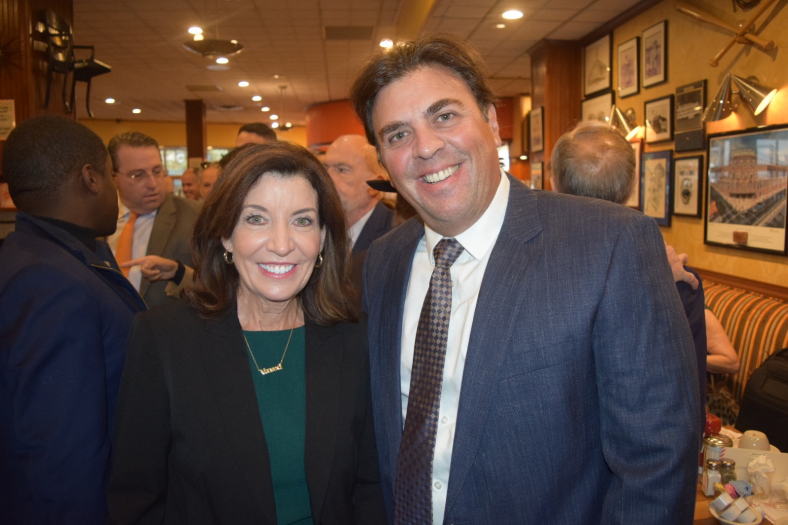 NY Gov. Hochul broadly smiling, dressed in business attire, posing with Richard Klass, broadly smiling, dressed in business attire, in restaurant.