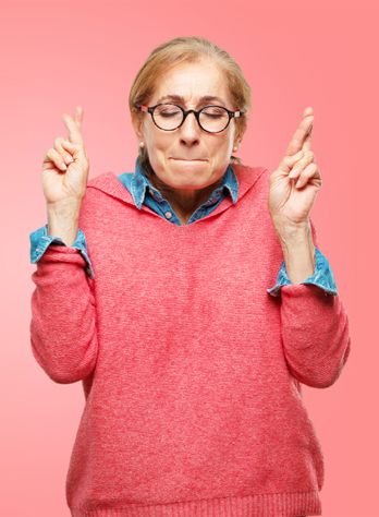 woman with glasses, wearing pink and blue, with fingers crossed and eyes closed - illustrating article by Richard Klass about default under the terms of a Promissory Note.