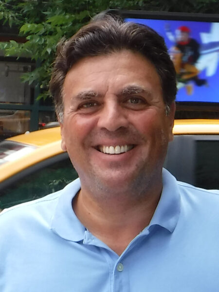 Richard A. Klass, Esq., Principal, headshot. Dressed casually in a light blue polo shirt and standing near a taxi.
